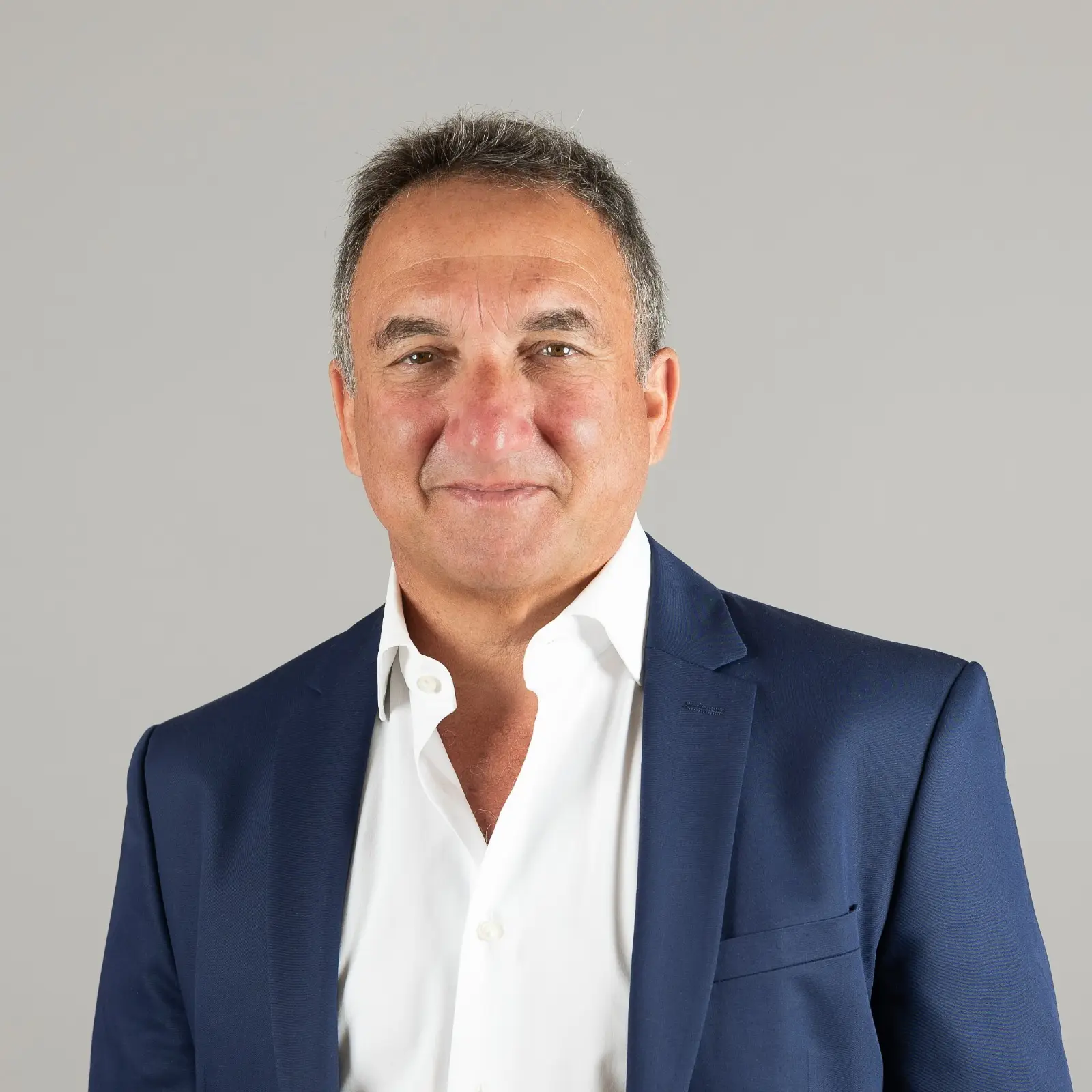 Portrait de Philippe Lugassy, souriant, en chemise blanche et veste bleu marine